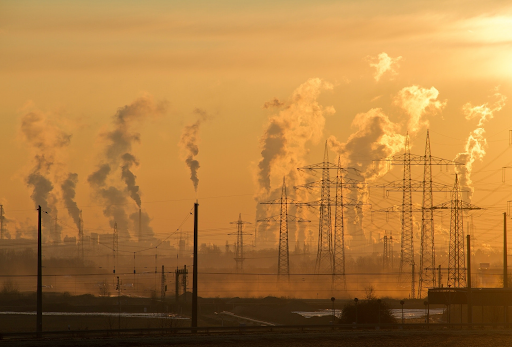 Landscape photo with several transmission towers in the mid ground and smoke stacks in the background. 